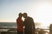Vista laterale da vicino di un uomo e di una donna caucasici maturi abbracciati dal mare — Foto stock