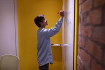 Seitenansicht eines jungen kaukasischen Mannes, der auf einem Whiteboard schreibt, während er im Büro eines kreativen Unternehmens Brainstorming betreibt — Stockfoto
