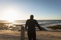 Vista trasera de un hombre caucásico maduro admirando la vista por el mar al atardecer - foto de stock