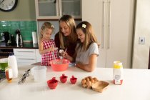 Vista frontal de una joven mujer caucásica cocinando con sus hijas adolescentes y más jóvenes en su cocina - foto de stock