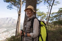 Porträt einer reifen kaukasischen Frau mit Nordic-Walking-Stöcken in der Hand und lächelnd in die Kamera, die Landschaft hinter sich — Stockfoto