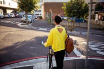 Raer vue d'un jeune transgenre de race mixte à la mode adulte dans la rue, debout et tenant un vélo — Photo de stock