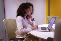 Вид збоку крупним планом молода змішана жінка, що працює в офісі креативного бізнесу, сидить за столом за допомогою ноутбука — стокове фото