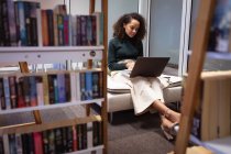 Вид спереди молодой женщины смешанной расы, сидящей в лофте, работающей за ноутбуком в офисе креативного бизнеса — стоковое фото