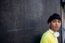 Vista frontal de un joven transgénero mestizo de moda en la calle, contra una pared gris - foto de stock