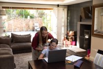 Front view of a young Caucasian pregnant woman standing behind her tween daughter using a laptop computer in their dining room — Stock Photo