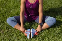 Вид спереди Низкая часть женщины в спортивной одежде сидит на траве, держа ноги и растягиваясь во время тренировки в парке — стоковое фото