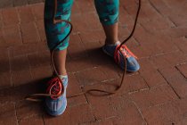 Sección baja de las piernas y los pies de la mujer que usa ropa deportiva sosteniendo una cuerda durante un entrenamiento en un día soleado en un parque - foto de stock
