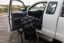 Rear view of a young Caucasian man in a wheelchair by his pick-up truck, parked in a car park with the door open — Stock Photo