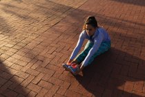 Erhöhte Ansicht einer jungen kaukasischen Frau in Sportkleidung, die sich hinsetzt und ihre Knöchel hält, während sie in einem Park trainiert — Stockfoto