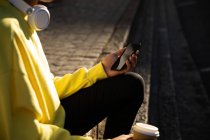 Вид сбоку на среднюю часть модного мужчины на улице, держащего смартфон и чашку кофе — стоковое фото
