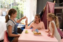 Front view of a young Caucasian woman with her tween and younger daughters having a dolls tea party at home — стокове фото