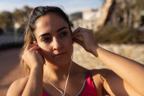 Vista frontale primo piano di una giovane donna caucasica che indossa abiti sportivi mettendo in auricolari prima di correre in un parco — Foto stock