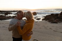 Vista lateral de um homem e uma mulher caucasianos maduros dançando juntos em uma praia ao pôr do sol — Fotografia de Stock