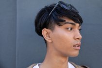 Vista laterale di un giovane transgender alla moda di razza mista adulto in strada, contro un muro grigio — Foto stock
