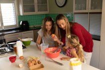 Front view of a young Caucasian woman cooking with her tween and younger daughters in their kitchen — стокове фото