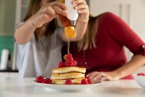 Front view of a young Caucasian woman making pancakes in the kitchen at home with her tween — Stock Photo