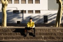 Vue de face d'un jeune transgenre mixte à la mode adulte dans la rue, assis sur des marches — Photo de stock