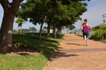 Visão traseira de uma jovem caucasiana vestindo roupas esportivas correndo em um caminho durante um treino em um dia ensolarado em um parque — Fotografia de Stock