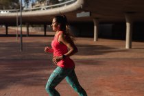 Vista lateral close-up de uma jovem caucasiana vestindo roupas esportivas correndo durante um treino em um dia ensolarado em um parque — Fotografia de Stock