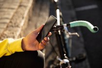 Gros plan d'une main d'un homme à la mode dans la rue, tenant un smartphone à côté d'un vélo — Photo de stock