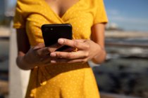 Vue de face gros plan de la femme utilisant un smartphone par une journée ensoleillée au bord de la mer — Photo de stock