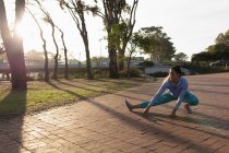 Vorderansicht einer jungen kaukasischen Frau in Sportkleidung, die sich hinhockt und den Boden mit einem Bein ausstreckt, während sie in einem Park trainiert — Stockfoto