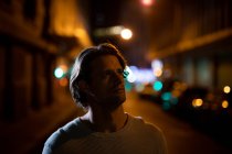 Close up front view of a young Caucasian man standing in a street at night, looking away — Stock Photo