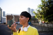 Seitenansicht eines modischen jungen Transgender-Erwachsenen mit gemischter Rasse auf der Straße, der mit Baskenmütze auf dem Smartphone spricht — Stockfoto