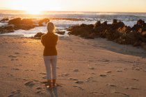 Rear view of a mature Caucasian woman admiring the view by the sea at sunset — Stock Photo