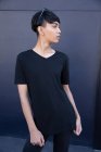 Seitenansicht einer modischen jungen gemischten Rasse Transgender-Erwachsene auf der Straße gegen eine graue Wand — Stockfoto