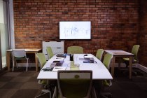 View of the modern office of a creative business, with a meeting table, desks, chairs and a monitor mounted on an exposed brick wall — Stock Photo