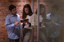 Передній погляд закриває вигляд молодої кавказької жінки і чоловіка, що стоять в офісі творчого бізнесу, дивлячись на планшетний комп'ютер разом з ним. — стокове фото