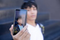 Vorderansicht einer modischen jungen gemischten Rasse Transgender Erwachsenen auf der Straße, zeigt Bildschirm des Smartphones, macht ein Selfie — Stockfoto