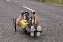 Front view of a young Caucasian man in sportswear on a recumbent bicycle cycling on a country road — Stock Photo