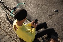 Vue d'angle HIgh d'un jeune adulte transgenre mixte à la mode dans la rue, envoyant un texto sur le smartphone portant un béret avec un vélo en arrière-plan — Photo de stock
