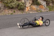 Вид сбоку на молодого кавказца в спортивной одежде на лежачем велосипеде на велосипеде по проселочной дороге, со скалами на заднем плане — стоковое фото