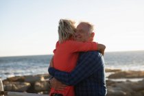Side view close up of a smiling mature Caucasian man and woman embracing during a walk by the sea — Stock Photo