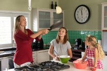 Vorderansicht einer jungen kaukasischen schwangeren Frau, die in der Küche zu Hause mit ihrer jüngeren Tochter Pfannkuchen backt — Stockfoto