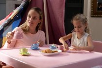 Vista frontal de una joven mujer caucásica y su hija pequeña teniendo una fiesta de té de muñecas en casa - foto de stock