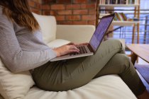 Vista lateral seção média da mulher usando um computador portátil sentado em um sofá na área de estar de um escritório criativo — Fotografia de Stock