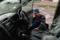Вид спереду крупним планом молодого Кавказького чоловіка вихід з машини в інвалідному візку на автостоянці в сільській місцевості — стокове фото