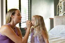 Side view close up of a young Caucasian woman putting make-up on her young daughter in her — Stock Photo