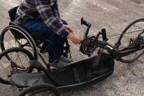 Low section of man in a wheelchair assembling a recumbent bicycle in a car park — Stock Photo