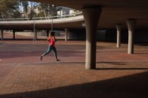 Вид сбоку на молодую кавказку в спортивной одежде, бегущую во время тренировки в солнечный день в парке — стоковое фото