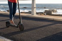 Vue latérale de près de la femme chevauchant un scooter e par la mer au coucher du soleil — Photo de stock