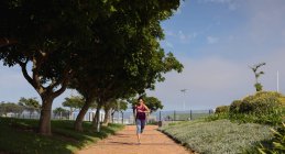 Вид спереди молодой белой женщины в спортивной одежде, бегущей по дорожке и смотрящей на свои умные часы во время тренировки в солнечный день в парке — стоковое фото