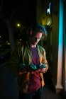 Front view close up of a young Caucasian man standing in a street at night using a smartphone by a lit shop window — Stock Photo