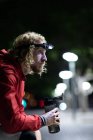 Seitenansicht eines jungen athletischen kaukasischen Mannes, der abends in einem Stadtpark trainiert, mit einem Scheinwerfer auf der Ruhepause und defokussierten Stadtlichtern im Hintergrund — Stockfoto