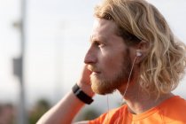 Vista lateral de perto de um jovem atlético caucasiano exercitando-se em uma passarela em uma cidade, ouvindo música com fones de ouvido em — Fotografia de Stock
